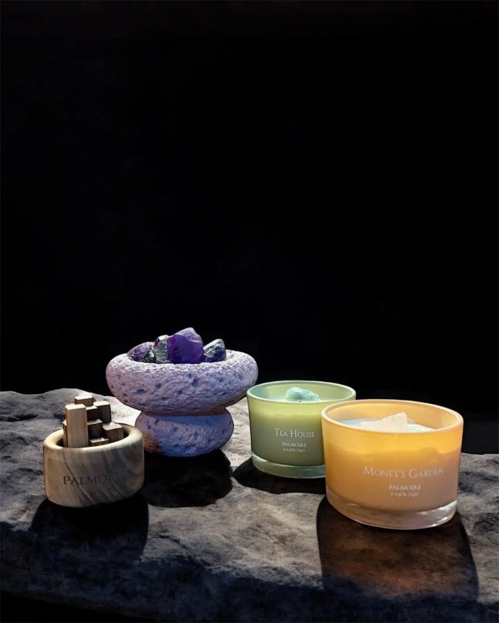 Zwei Duftkerzen und zwei Diffuser in verschiedenen Farben und Materialien sind auf einer flachen Oberfläche angeordnet, die jeweils Kristalle oder Steine enthalten, vor einem Hintergrund mit sanftem Farbverlauf.