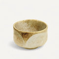 Die Fitaura Matcha Schale Chawan Yuki, handgemacht aus Raku Keramik, besticht durch ihre runde Form und eine gesprenkelte beige-braune Glasur - präsentiert vor weißem Hintergrund.