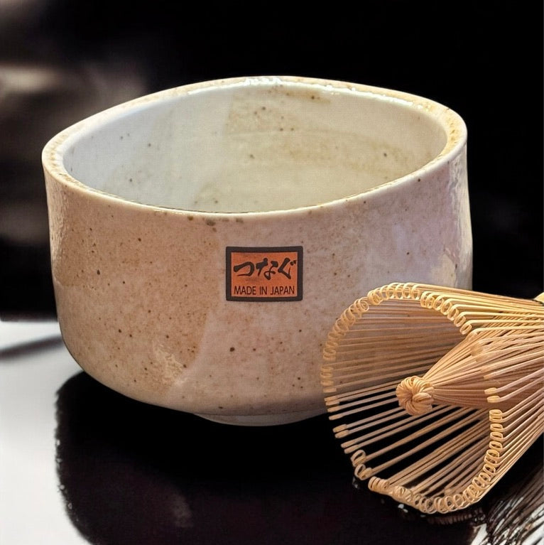 Eine handgemachte Matcha Schale Chawan Yuki aus Raku Keramik von Fitaura steht neben einem Bambus-Teebesen auf dunklem Untergrund.