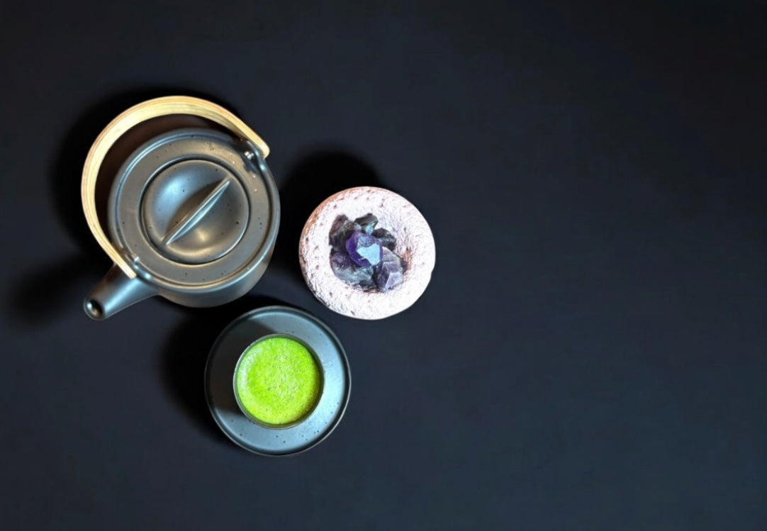 minimalistisches flatlay: matcha - tee in schwarzer schale, Keramik - Teekanne und steinschale mit Amethysten. Fitaura wohlbefinden.