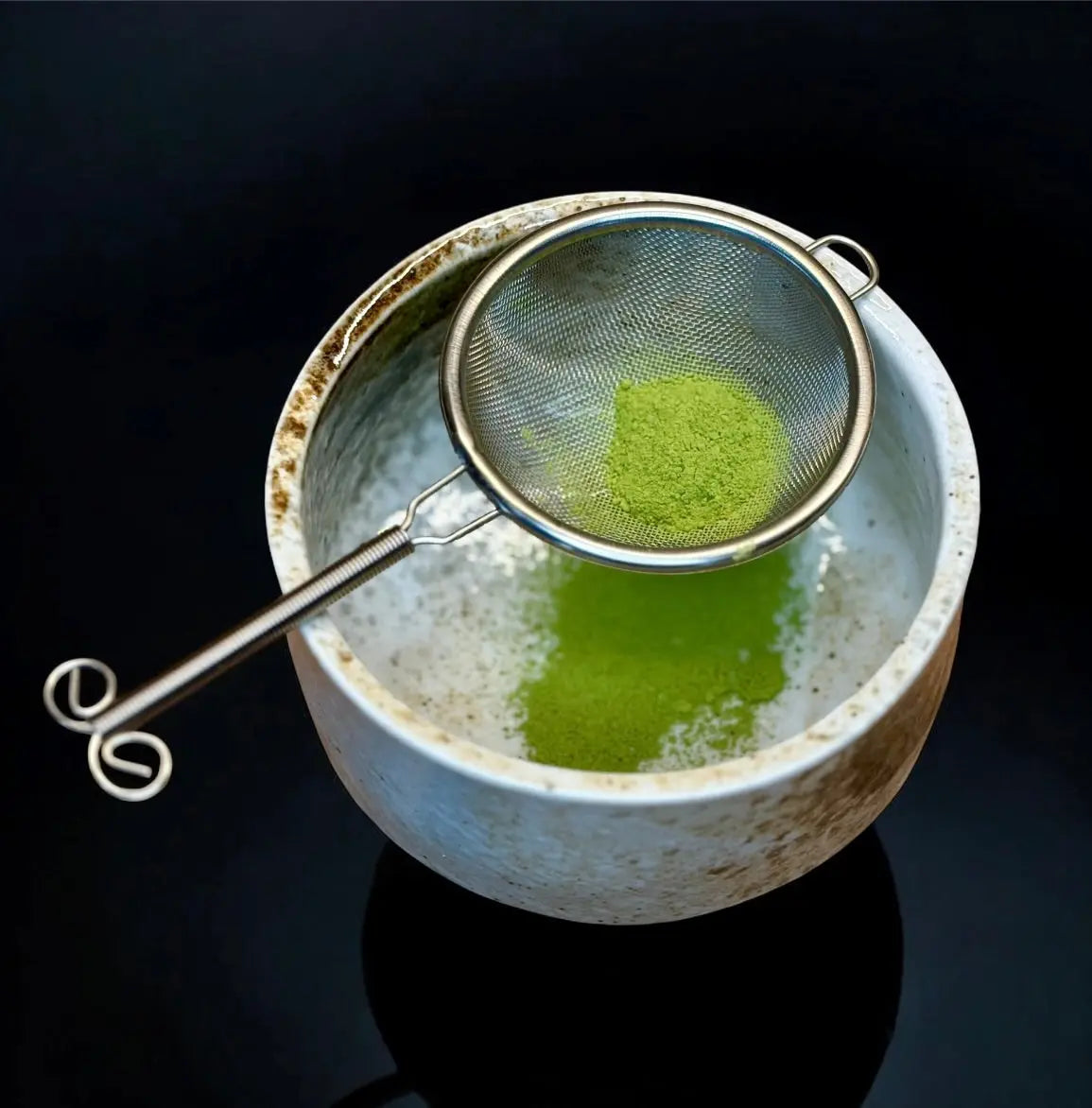 fein gesiebtes pulver im traditionellen Teesieb über Keramikschale